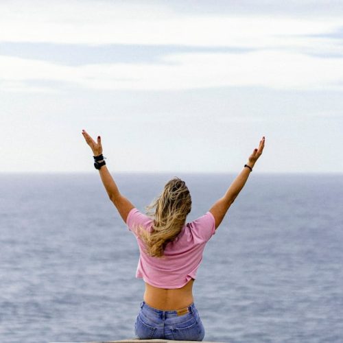 a woman with her arms raised in front of a body of water