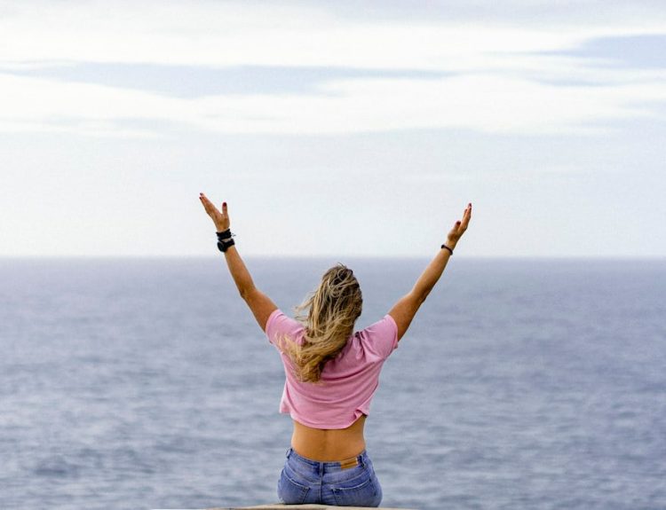 a woman with her arms raised in front of a body of water